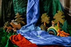 A small-world woodland laid out on silks: a blue river between green banks, wooden deer and foxes, a rabbit on a green arch, and wooden trees