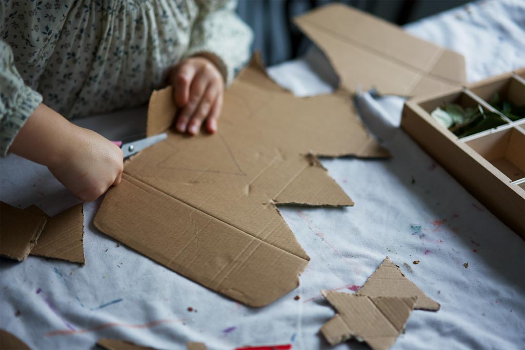 A child crawling through a cardboard box den lined with knitted blankets